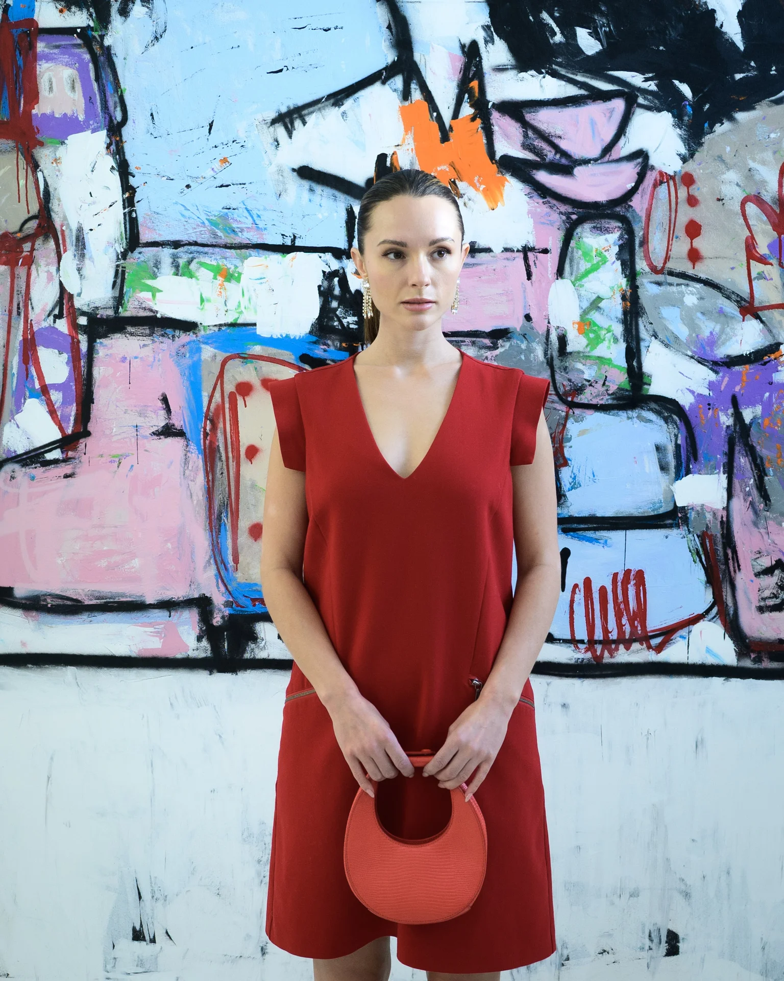 A woman in a vibrant red dress stands before a colorful abstract mural.
